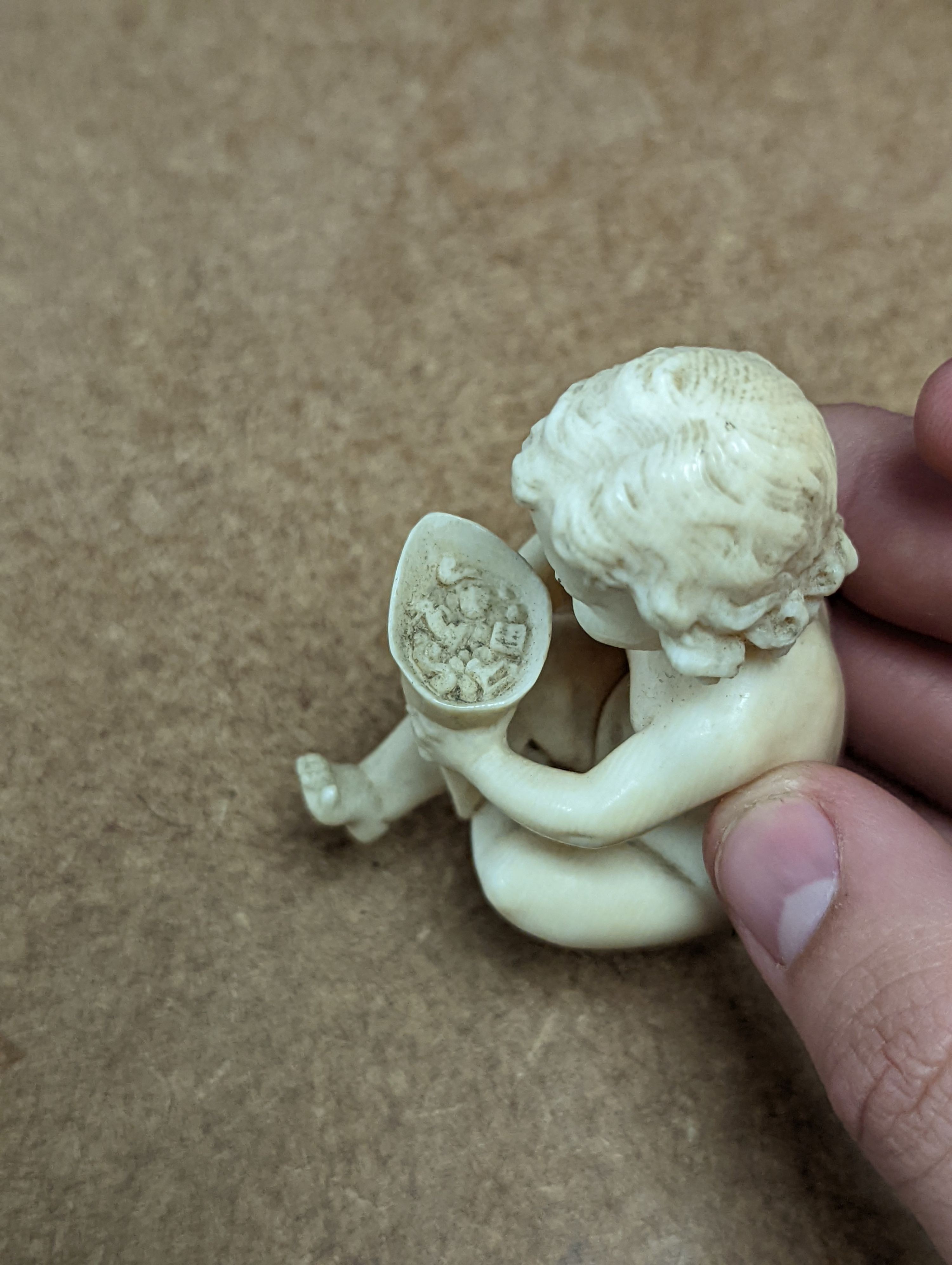 A 19th century Continental carved ivory figure of a child holding a cornucopia - 7cm tall